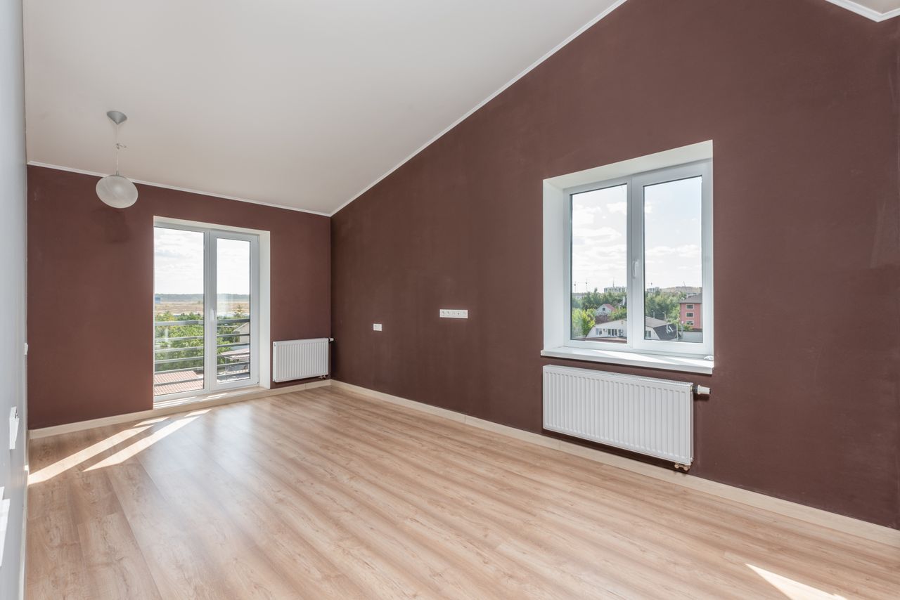 Bright and spacious beige room with brown walls, large windows, and a wooden floor.