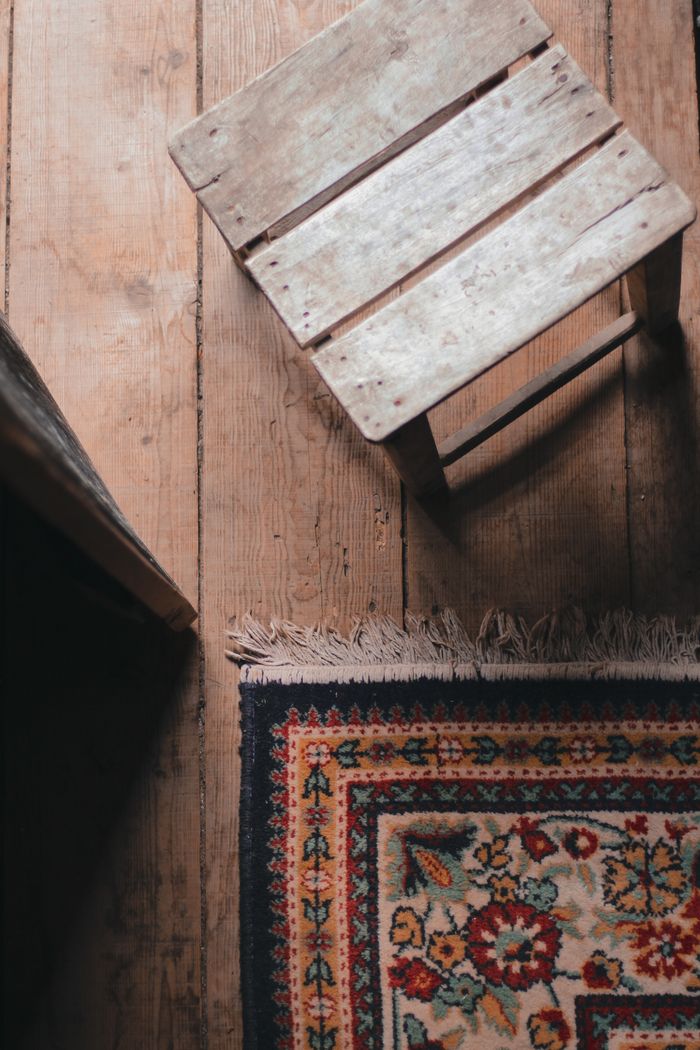 High angle of shabby wooden chair placed on withered floor near decorated carpet