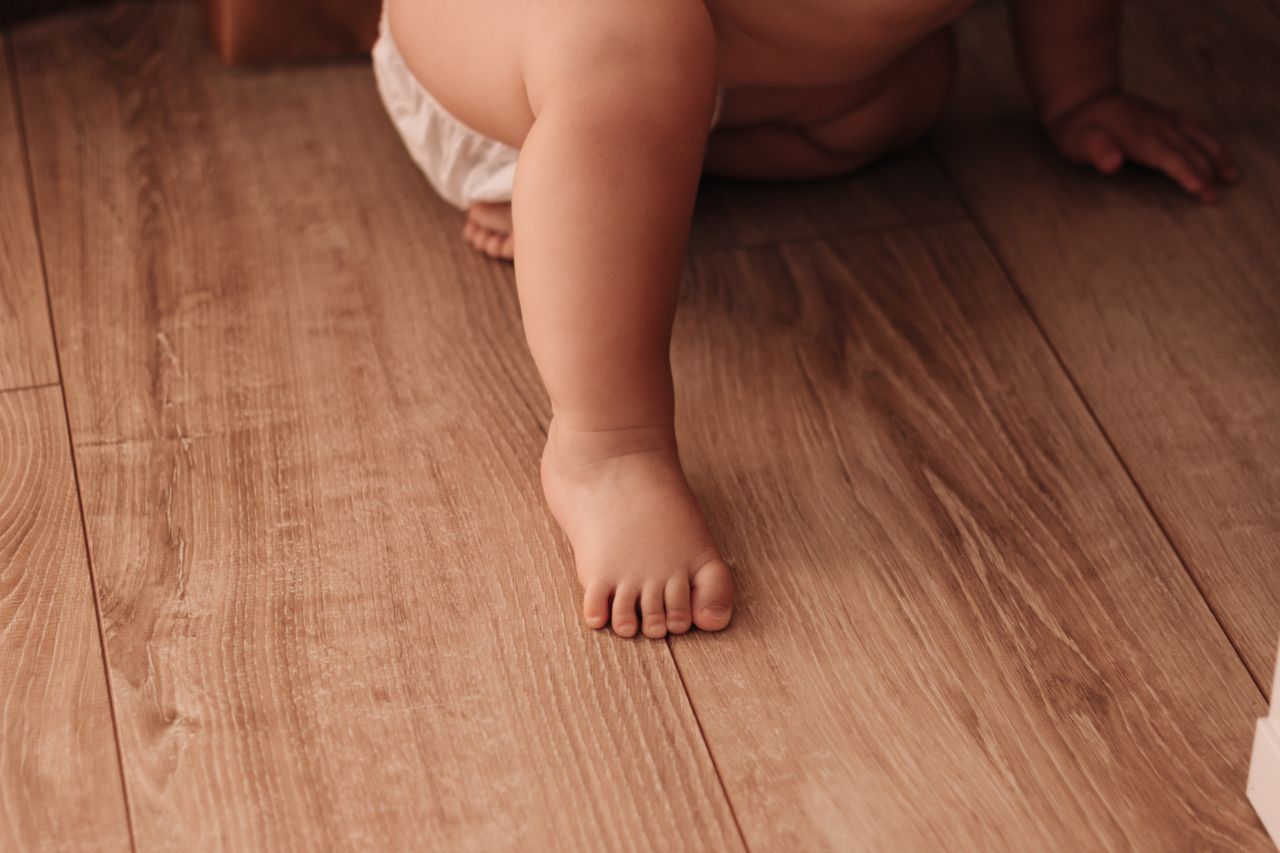 Close-up of a baby crawling indoors on a wooden floor, showcasing tiny feet and playful innocence.