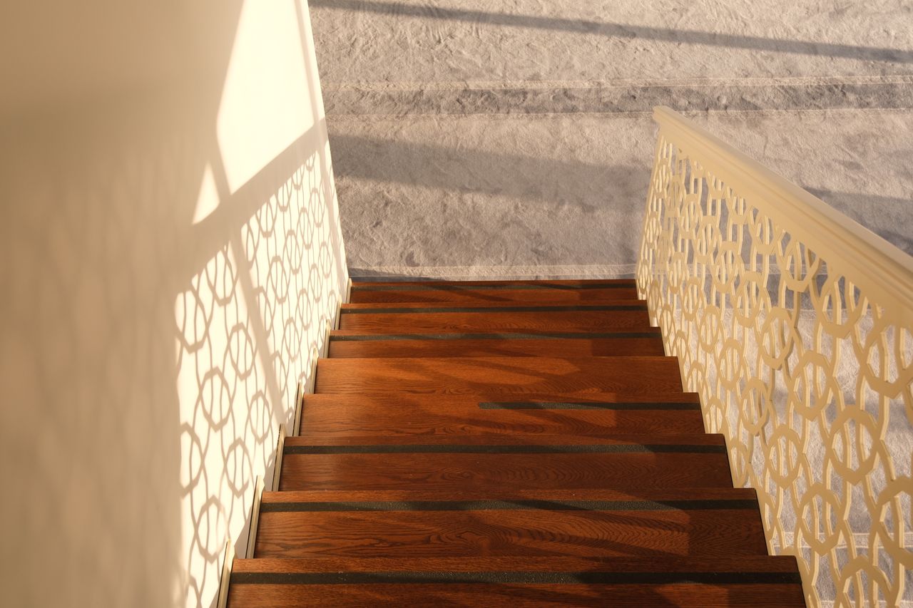 Elegant wooden stairs with intricate iron railing, basking in warm sunlight, casting artistic shadows.
